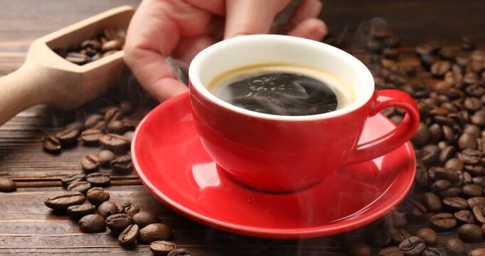 Woman putting cup with aromatic coffee onto wooden table with beans and scoop, closeup