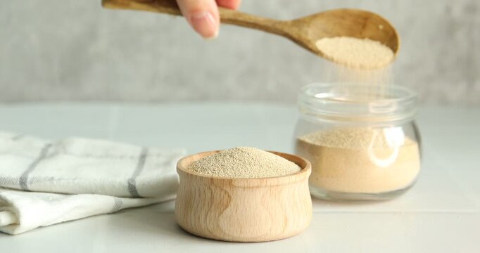 Woman pouring dry yeast into glass jar at white table, closeup