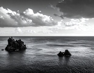 A monochrome ocean scene featuring two rocky islands jutting out of the calm water under a dramatic sky filled with clouds