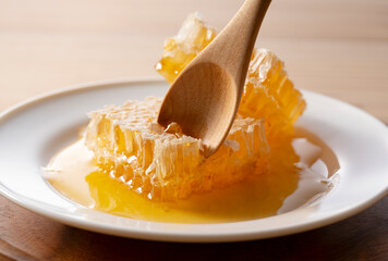 Scooping Fresh Organic Honeycomb from a White Plate with a Wooden Spoon, Delicious Raw Liquid Honey for Breakfast with Copy Space