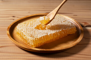 Scooping Fresh Raw Honey from Honeycomb with a Wooden Spoon, Natural Organic Superfood on Wooden Plate with Copy Space