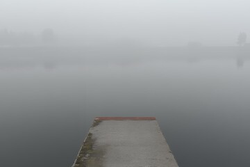 A concrete pier disappears into the dense fog over calm water