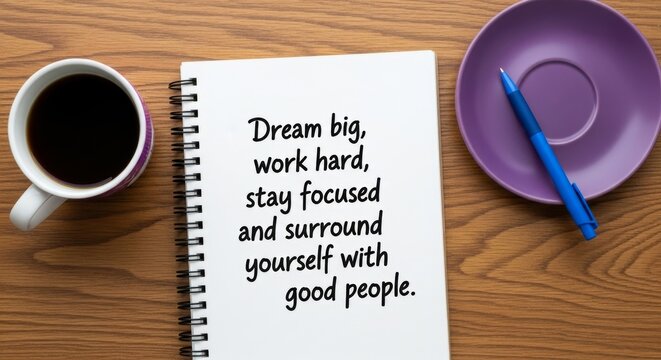 Spiral bound notebook with motivational quote 'Dream big, work hard, stay focused and surround yourself with good people' on a wooden table