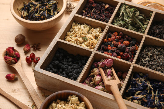 Box with different types of dry tea on wooden background, closeup
