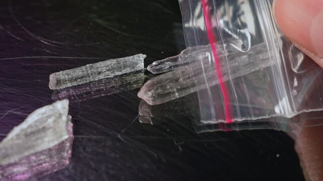 Synthetic opioid crystals like fentanyl or nitazenes drugs in clear plastic bag held in hands of drug user concept.