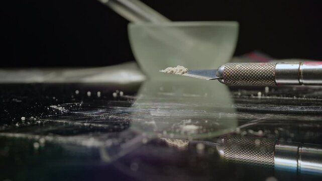 Drug addict&rsquo;s shaking hand holds craft knife blade taking a tip fentanyl on the blade concept. Two milligrams of fentanyl is lethal dose for humans. Tiny pile of powder to give a sense of scale.