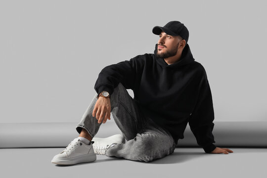 Young man in black hoodie with cap sitting on color background