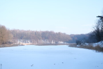 Lake reflection. Winter landscape during sunset. Trees covered with snow. Sun rays through the trees
