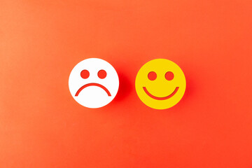 White sad face and yellow happy face emoji icons placed together on an orange background. Concept for customer feedback, satisfaction rating, emotional comparison, and business evaluation.