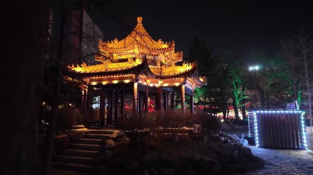 Smooth motion shot passing an illuminated Chinese pagoda at night in Lao Dong Park, Dalian. Traditional architecture glows against the dark sky, creating a calm, atmospheric urban landmark scene.