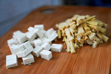Diced tofu with sliced bamboo shoots on wooden cutting board