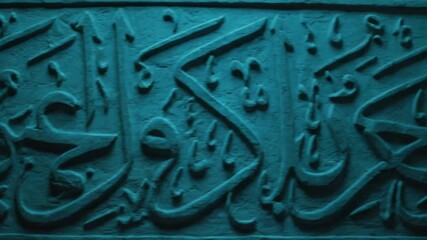 A captivating close-up reveals intricate, ancient script meticulously carved in relief onto a textured stone surface, bathed in a deep, mysterious blue-green light. The flowing, ornate characters evok