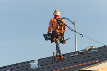 Construction worker installing HVAC ducts on the roof of a home under construction, representing residential building development and exterior mechanical installation