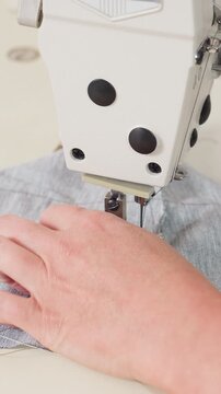closeup sewing machine stitching denim fabric, hands guiding needle with steady rhythm, industrial presser foot biting thick textile, bobbin and spool visible, neutral studio light, calm focused