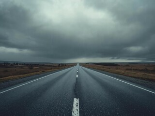 A long, straight road stretches into the distance under a dark, cloudy sky, passing through a vast, open landscape.