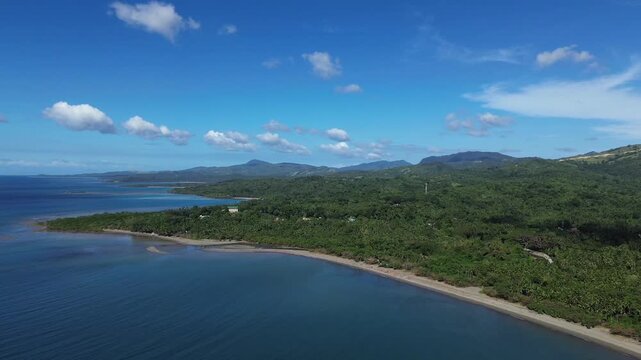 Aerial drone footage of a remote sandy beach on Tablas Island near Odiongan, Philippines, featuring dense green palm forest and rolling mountains in the background on a bright sunny day.