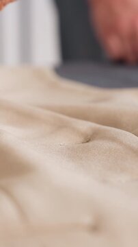 closeup white hands smoothing beige suede, inspecting tufted cushion surface on dark worktable, soft natural light, focused studio atmosphere, meticulous craftsmanship and texture study