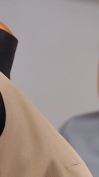 white maker testing beige fabric drape on mannequin, caucasian woman smooths shoulder and checks seam flow, closeup of zip and shoulder area, handson product development in bright studio, tactile