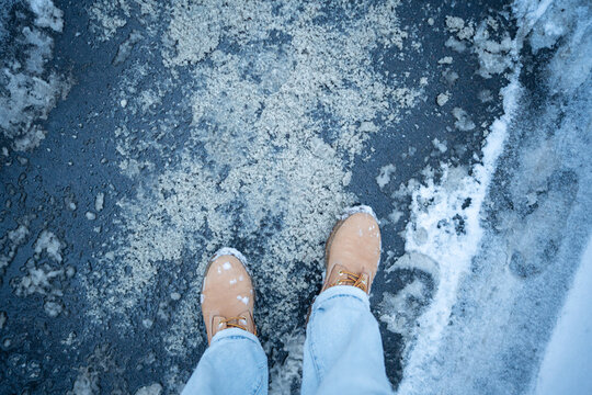 Person standing in middle of asphalt sidewalk covered in snow and technical salt, pavement coated with mixture of wet snow and special chemicals for ice crust formation prevention and safety reasons.