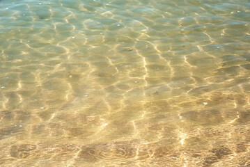 Clear sea water surface with ripples and sand background
