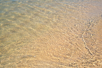 Clear sea water surface with ripples and sand