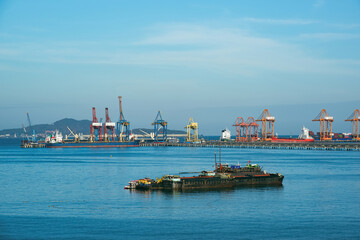 Industrial cargo port terminal with gantry cranes and tugboat in blue sea