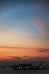 Silhouette of industrial cargo port cranes against dramatic twilight sky
