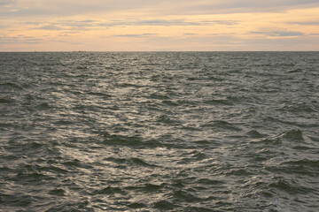 A wide shot of the ocean surface under a sky with soft clouds and a warm
