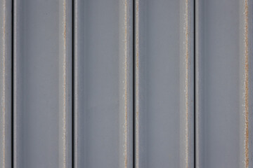 close-up, full-frame shot of a gray corrugated metal sheet with a row of rusty bolts.