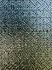 Close-up of patterned, opaque glass featuring a repetitive, embossed floral or cloverleaf design, with light filtering through