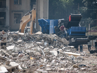 Demolition site showing excavators and workers clearing large piles of concrete rubble and construction debris. Large-scale construction waste management in China