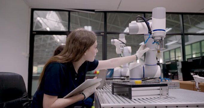 young female engineer inspects robotic arm operation while interacting with cobot using tablet device during smart factory automation training program focused on installation and control process