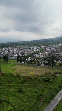 An aerial view of housing development in Wonosobo, showing neat rows of newly built homes, quiet streets, green open land, and a growing residential area blending with the surrounding landscape.