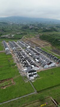 An aerial view of housing development in Wonosobo, showing neat rows of newly built homes, quiet streets, green open land, and a growing residential area blending with the surrounding landscape.