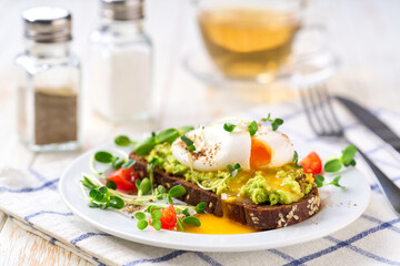 Toast with avocado and egg with cup of tea for healthy breakfast or snack. Sandwich with avocado and poached egg on a white table, selective focus.