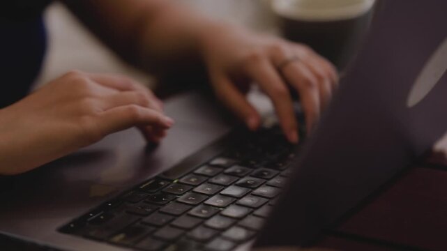 Close up female hands typing on computer sitting in the office. Young women working on laptop at home while drinking coffee at home. Technology lifestyle concept. Woman typing on laptop.