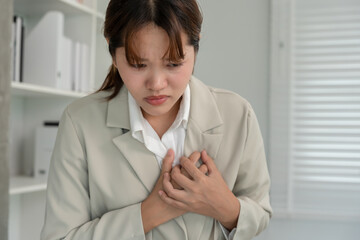 hand hold chest with heart attack symptoms, business woman working hard have chest pain caused by heart disease, leak, dilatation, enlarged coronary heart, press on the chest with painful expression