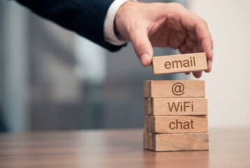 Businessman hand placing wooden block labeled email on stack with wifi and chat for communication