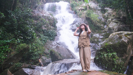 Portrait image of a woman standing in front of the waterfall in the forest