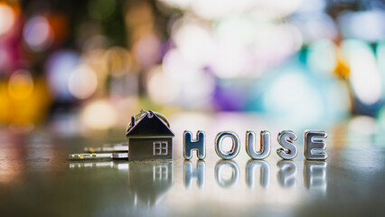 Miniature house with keys and house text on reflective surface with colorful bokeh background, representing real estate, home ownership, property investment, mortgage, rental, housing security.
