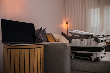 Online travel booking and digital nomad concept with laptop, suitcase and airplane model in modern living room