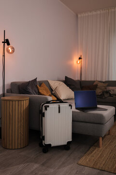 Laptop on sofa next to hard shell suitcase in a cozy modern living room