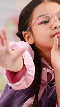 Young Schoolgirl with Pink Glasses Making a Stop Gesture in Classroom