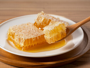 Fresh Honeycomb with Wooden Spoon and Dripping Raw Honey on White Plate over Wooden Table