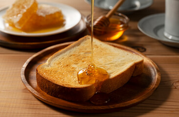Honey Drizzling on Toast Bread on Wooden Plate with Honeycomb and Honey Dipper