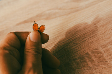Close up of hand holding a small red heart pendant over a rustic wooden table background, concept of vintage love, memory, and handmade gift.