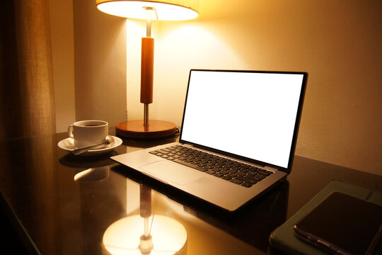 Cozy modern workspace with laptop coffee cup smartphone and warm lamp light on reflective glass desk - Powered by Adobe