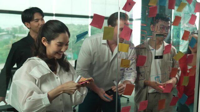 Happy professional business team brainstorming marketing idea by using colorful sticky notes to share creative idea at glass wall. Group of diverse business team discuss about strategy. Manipulator.