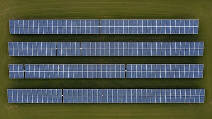 Aerial view of four rows of solar panels on a green field with a grid pattern