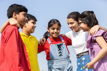 Happy group of indian kids friends embracing and sharing a candid conversation together in summer park, concept of teamwork and friendship. Children having fun talking and discussing outdoor. © GAJENDRRA BHATI 